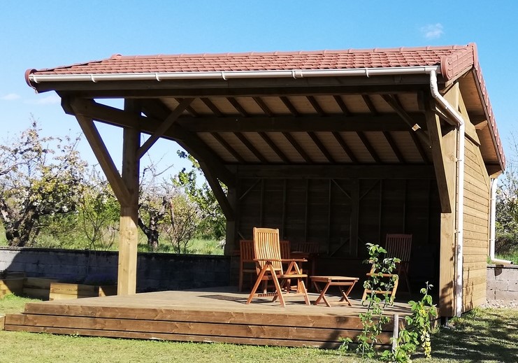 préau en bois avec toiture en tuiles rouges abritant un salon de jardin