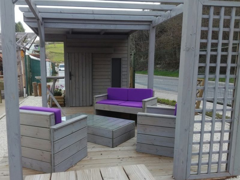 vue du salon de jardin en bois lasuré en gris avec des coussins violets