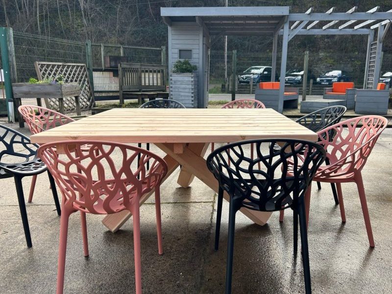 table en bois carrée avec des pieds croisés et ses chaises en plastique